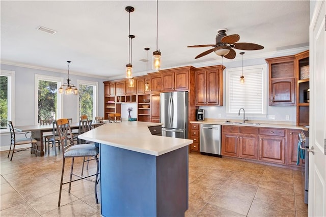 kitchen with appliances with stainless steel finishes, ceiling fan with notable chandelier, sink, pendant lighting, and a center island