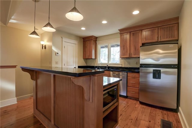 kitchen featuring pendant lighting, a kitchen island, appliances with stainless steel finishes, light hardwood / wood-style floors, and a breakfast bar area