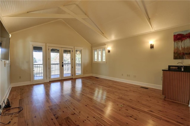 unfurnished living room featuring a healthy amount of sunlight, wood-type flooring, beam ceiling, and french doors