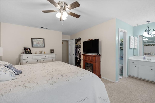 bedroom with a closet, light colored carpet, visible vents, connected bathroom, and ceiling fan with notable chandelier