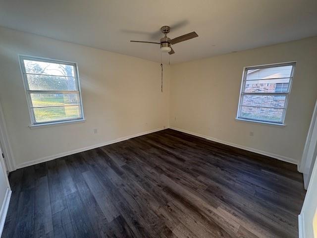 unfurnished room featuring dark wood-style flooring, a ceiling fan, and baseboards