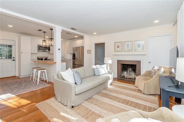 living area featuring a fireplace, visible vents, light wood finished floors, and recessed lighting
