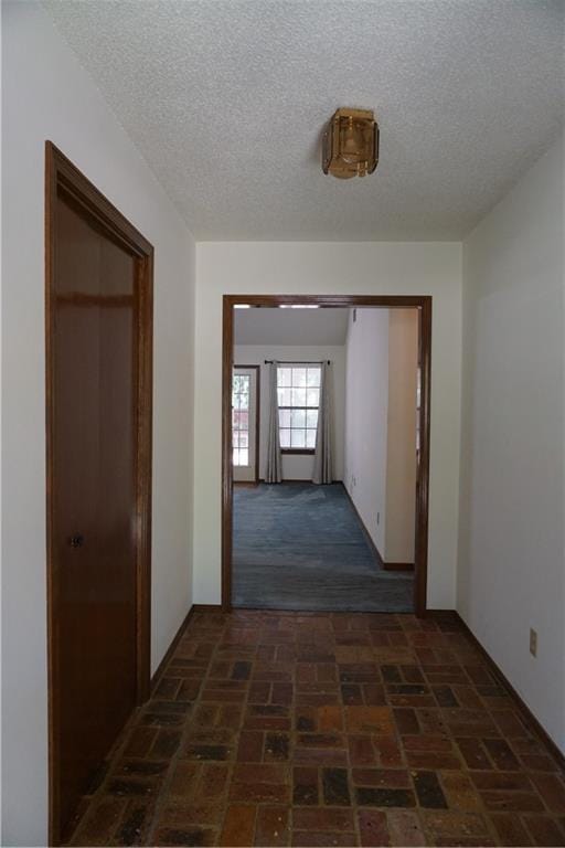 corridor with a textured ceiling, brick floor, and baseboards
