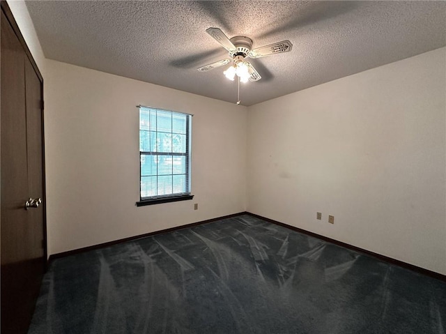 empty room with baseboards, dark carpet, ceiling fan, and a textured ceiling