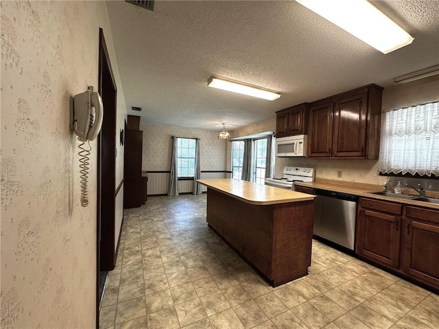 kitchen with a center island, dark brown cabinets, a sink, a textured ceiling, and white appliances