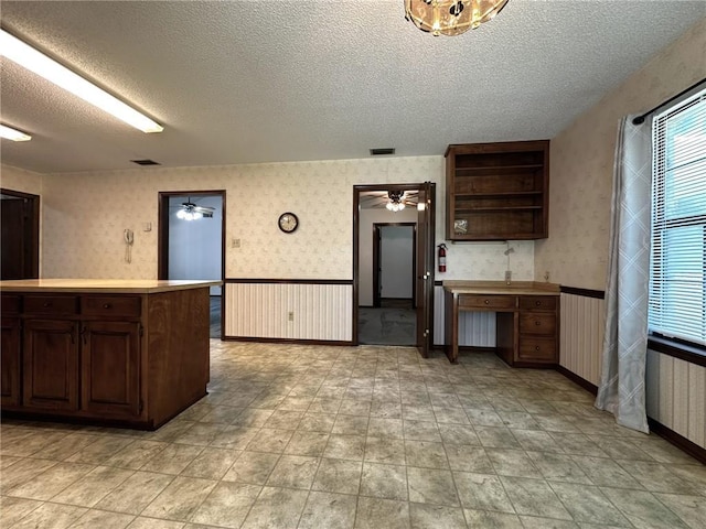 kitchen with wallpapered walls, a textured ceiling, and a wainscoted wall