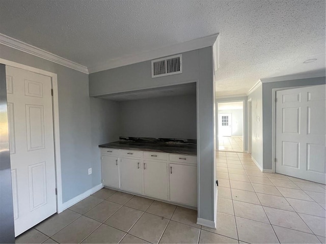 kitchen with white cabinetry, ornamental molding, light tile patterned flooring, and a textured ceiling