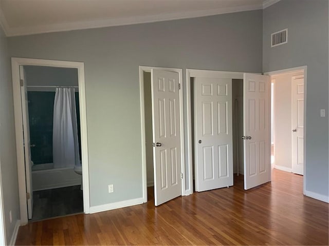 unfurnished bedroom featuring wood-type flooring, ornamental molding, two closets, and ensuite bathroom