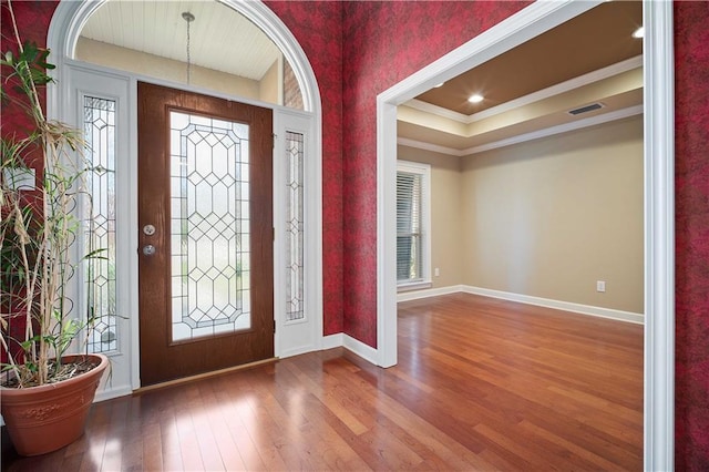 foyer featuring visible vents, baseboards, ornamental molding, wood finished floors, and a raised ceiling