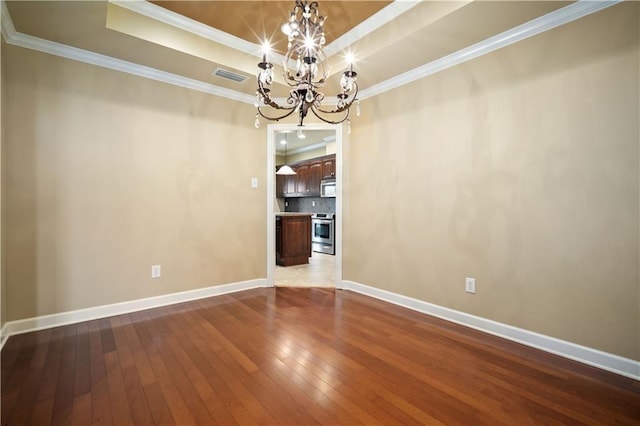 unfurnished room featuring visible vents, wood-type flooring, an inviting chandelier, crown molding, and a raised ceiling