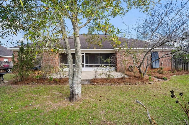 ranch-style home with a front lawn, brick siding, a sunroom, and roof with shingles