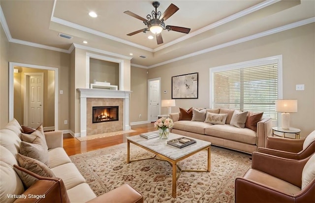 living area with a tray ceiling, crown molding, visible vents, and light wood-type flooring