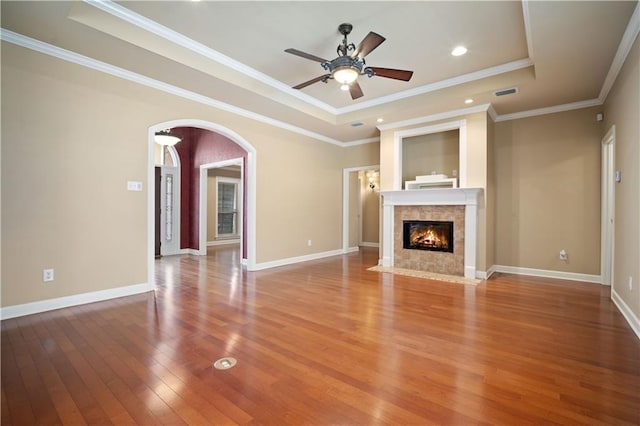 unfurnished living room with a tray ceiling, arched walkways, baseboards, and light wood-style flooring