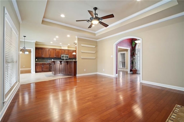 unfurnished living room with crown molding, a raised ceiling, baseboards, and hardwood / wood-style flooring