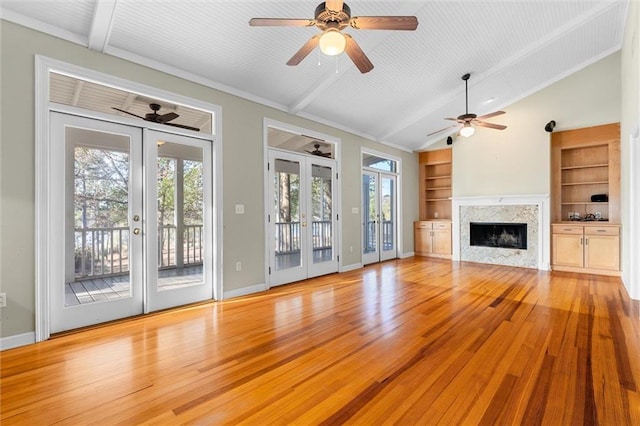 unfurnished living room featuring built in shelves, a premium fireplace, french doors, and light hardwood / wood-style flooring