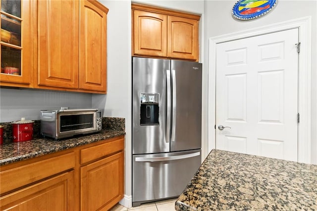 kitchen with light tile patterned floors, stainless steel fridge with ice dispenser, and dark stone counters