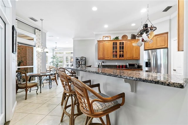 kitchen with a breakfast bar area, ornamental molding, stainless steel fridge, and dark stone counters