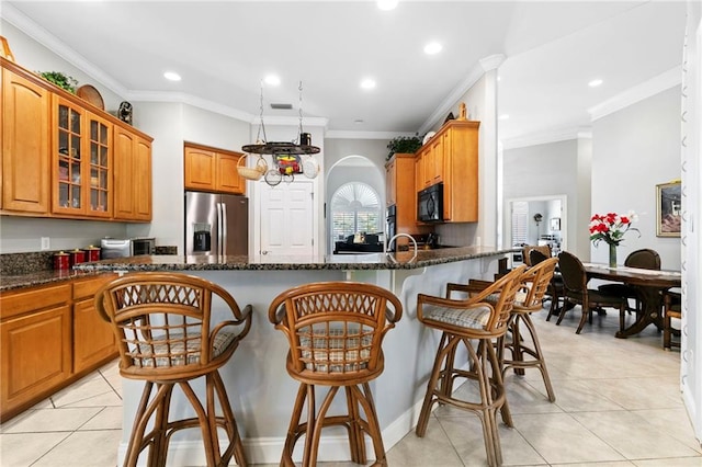 kitchen with kitchen peninsula, stainless steel refrigerator with ice dispenser, dark stone countertops, crown molding, and a breakfast bar