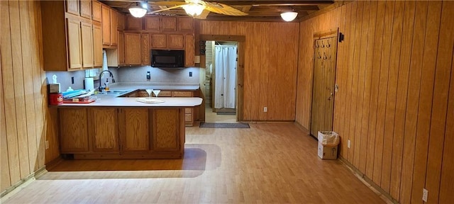 kitchen with wood walls, light wood-type flooring, kitchen peninsula, ceiling fan, and sink