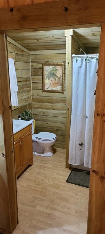 bathroom featuring toilet, hardwood / wood-style flooring, wood walls, wooden ceiling, and vanity