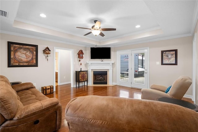 living room with crown molding, wood-type flooring, a raised ceiling, and ceiling fan