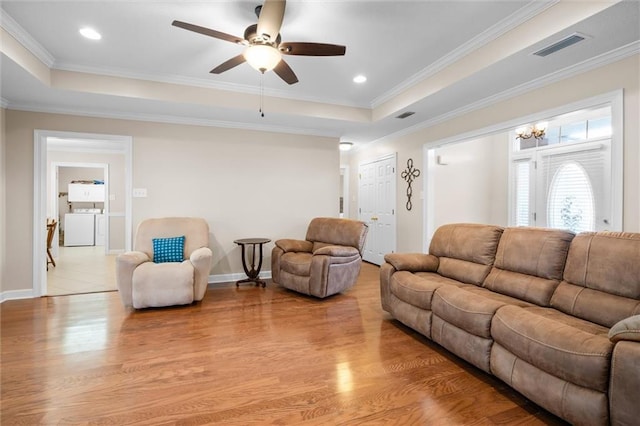 living room featuring crown molding, washer and dryer, light hardwood / wood-style flooring, and a tray ceiling