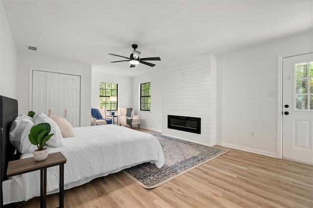 bedroom with a large fireplace, light wood-style floors, visible vents, and baseboards