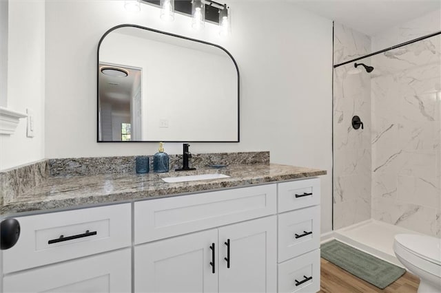 bathroom with toilet, a marble finish shower, wood finished floors, and vanity