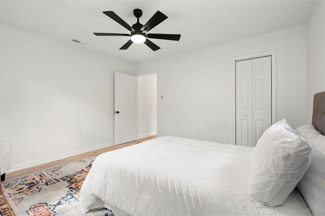 bedroom with wood finished floors, a closet, ceiling fan, baseboards, and visible vents