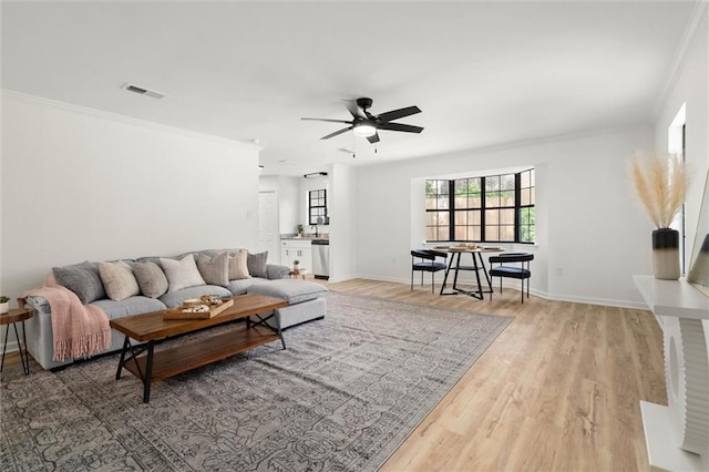 living area featuring crown molding, visible vents, ceiling fan, baseboards, and wood finished floors