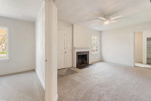 unfurnished living room with ceiling fan, light colored carpet, a tile fireplace, and a textured ceiling