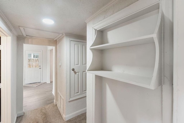 corridor with ornamental molding, light carpet, and a textured ceiling