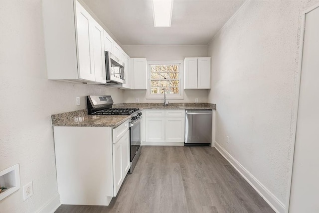 kitchen featuring sink, light hardwood / wood-style flooring, appliances with stainless steel finishes, white cabinets, and dark stone counters