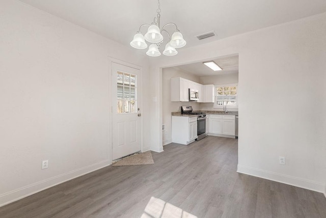 interior space with appliances with stainless steel finishes, hardwood / wood-style floors, white cabinets, decorative light fixtures, and a chandelier