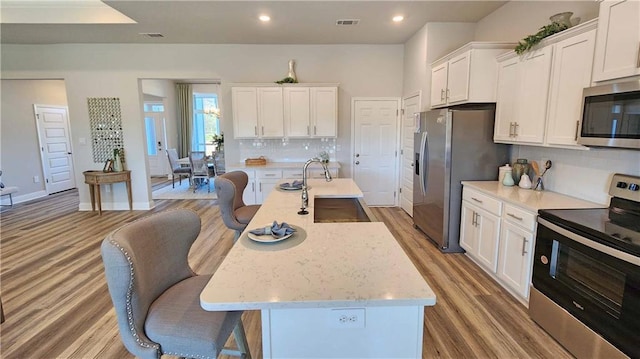 2295 Nadine Ln, Mobile, AL 36695 - kitchen featuring appliances with stainless steel finishes, white cabinetry, wood finished floors, decorative backsplash, and a kitchen breakfast bar