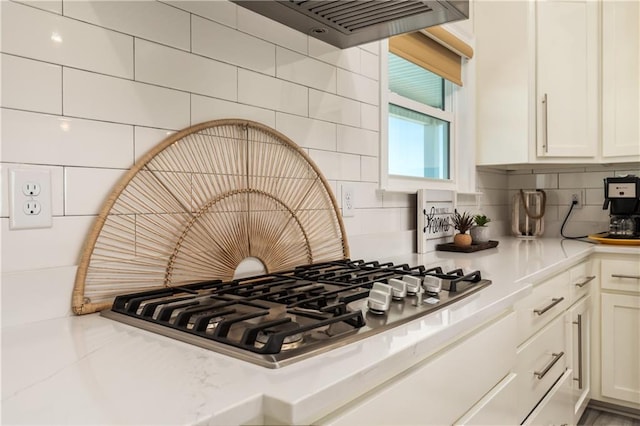 room details with range hood, light stone countertops, stainless steel gas stovetop, white cabinets, and backsplash