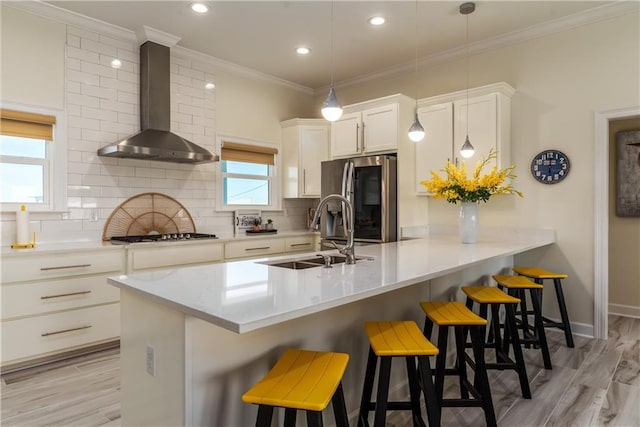 kitchen with a sink, backsplash, gas stovetop, stainless steel fridge with ice dispenser, and wall chimney range hood