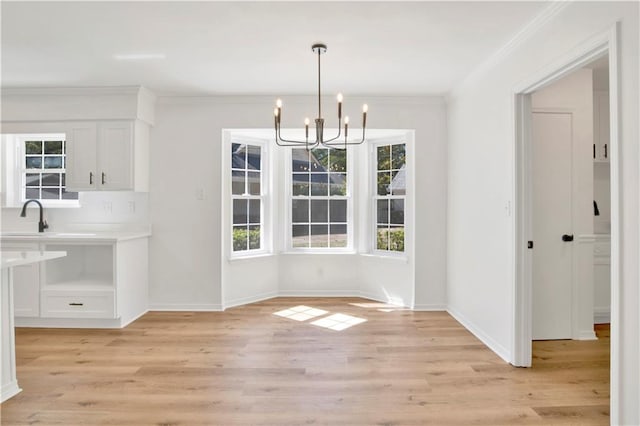 unfurnished dining area with ornamental molding, sink, light hardwood / wood-style floors, and a notable chandelier