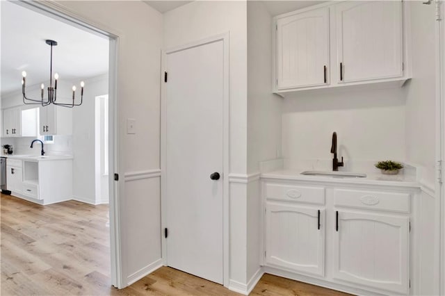 bar featuring decorative light fixtures, sink, white cabinets, stainless steel dishwasher, and light hardwood / wood-style floors