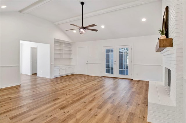 unfurnished living room featuring a fireplace, light wood-type flooring, ceiling fan, beam ceiling, and french doors