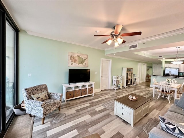 living room featuring visible vents, light wood-style flooring, ceiling fan, ornamental molding, and a tray ceiling