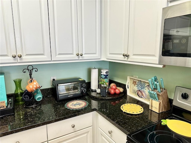 kitchen featuring a toaster, white cabinetry, stainless steel appliances, and dark stone counters