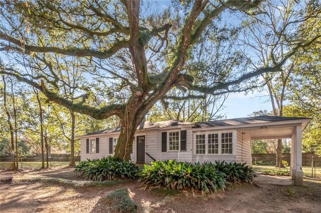 ranch-style home with dirt driveway, a carport, and fence