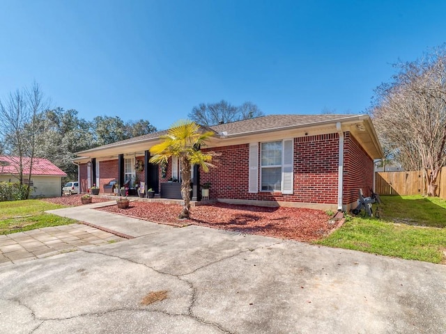 ranch-style house featuring brick siding, a porch, a front yard, and fence