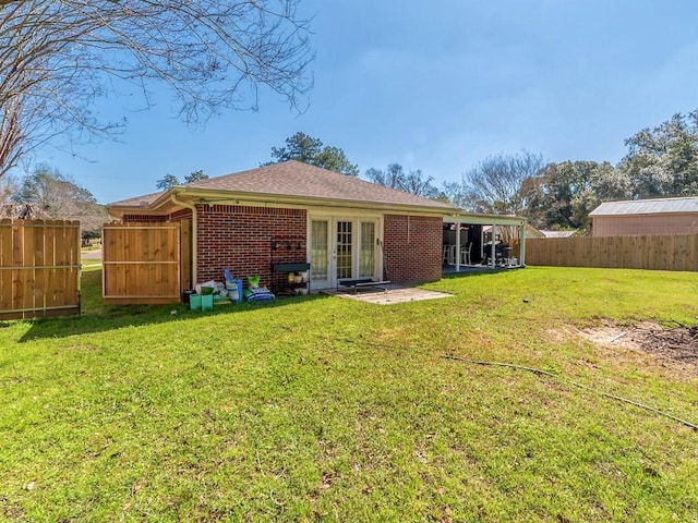 rear view of property with a shingled roof, brick siding, a yard, and a fenced backyard