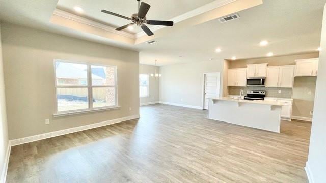 kitchen with a raised ceiling, light wood-type flooring, an island with sink, appliances with stainless steel finishes, and white cabinetry