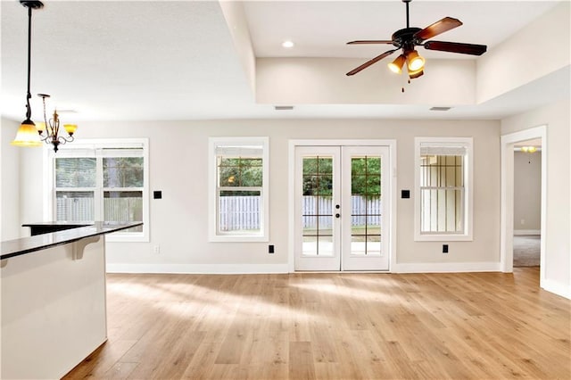 unfurnished living room with ceiling fan with notable chandelier, french doors, light wood-type flooring, and a raised ceiling