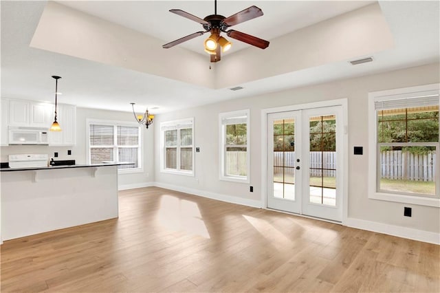 unfurnished living room featuring a tray ceiling, a wealth of natural light, french doors, and light hardwood / wood-style flooring