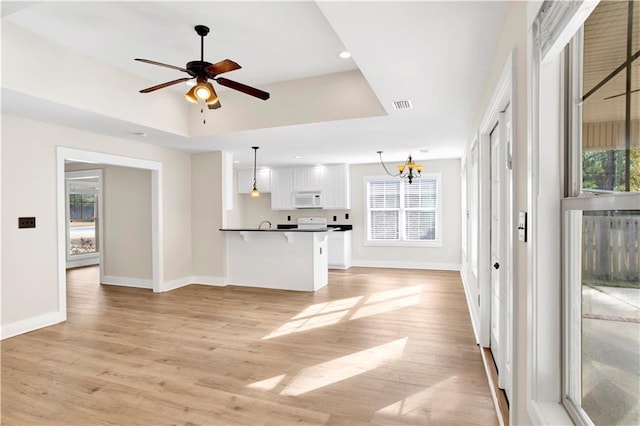 unfurnished living room featuring ceiling fan with notable chandelier and light hardwood / wood-style flooring