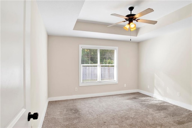 carpeted empty room featuring ceiling fan and a raised ceiling